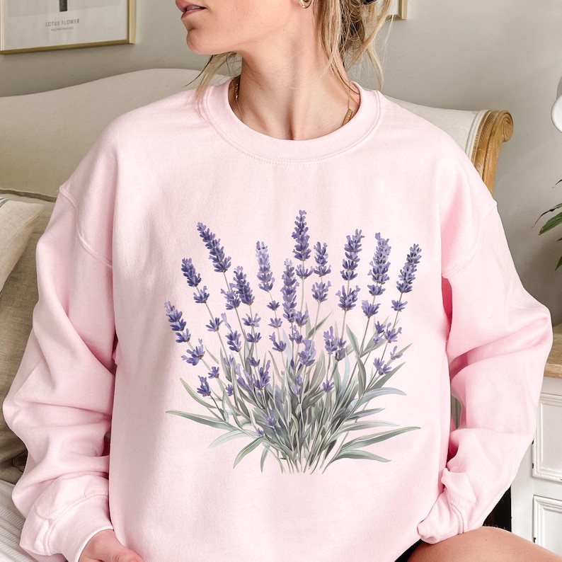 Op de afbeelding: Een roze sweatshirt met een lavendelbloemendruk. De bloemen zijn paars en groen.