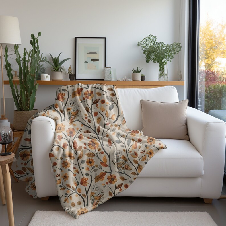 May include: A soft throw blanket with a cream background and a repeating pattern of owls, flowers, and leaves in shades of orange, brown, and gray.