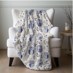 May include: A soft, cream-colored throw blanket with a repeating pattern of blue owls, leaves, and crescent moons.