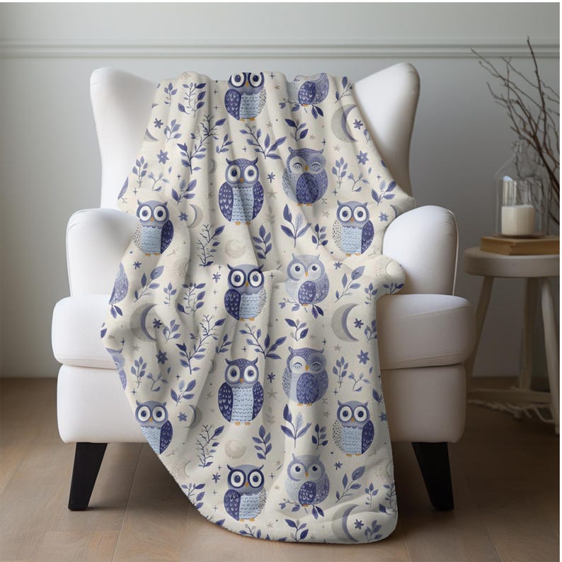 May include: A soft, cream-colored throw blanket with a repeating pattern of blue owls, leaves, and crescent moons.