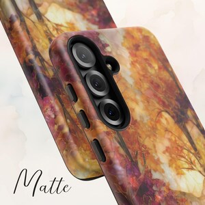 May include: Matte phone case featuring a colorful autumn forest design in shades of orange, red, and gold. The case has a triple-lens camera cutout and side buttons. The word "Matte" is written in a cursive font at the bottom.