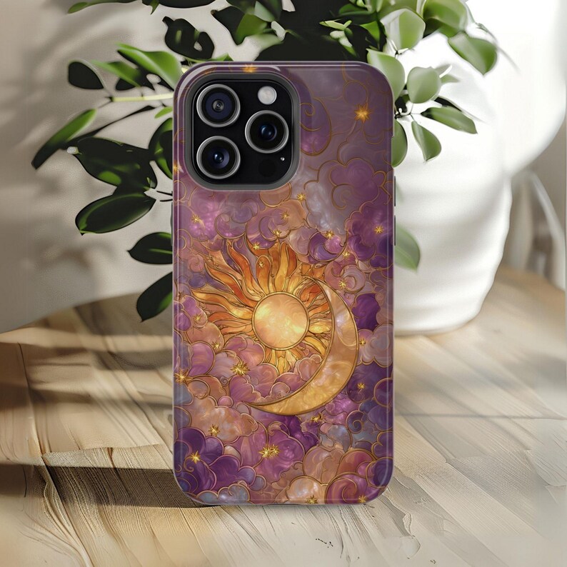 May include: A phone case with a celestial design. It features a golden sun and crescent moon set against a backdrop of purple clouds and stars. The case has a glossy finish and a protective bumper.