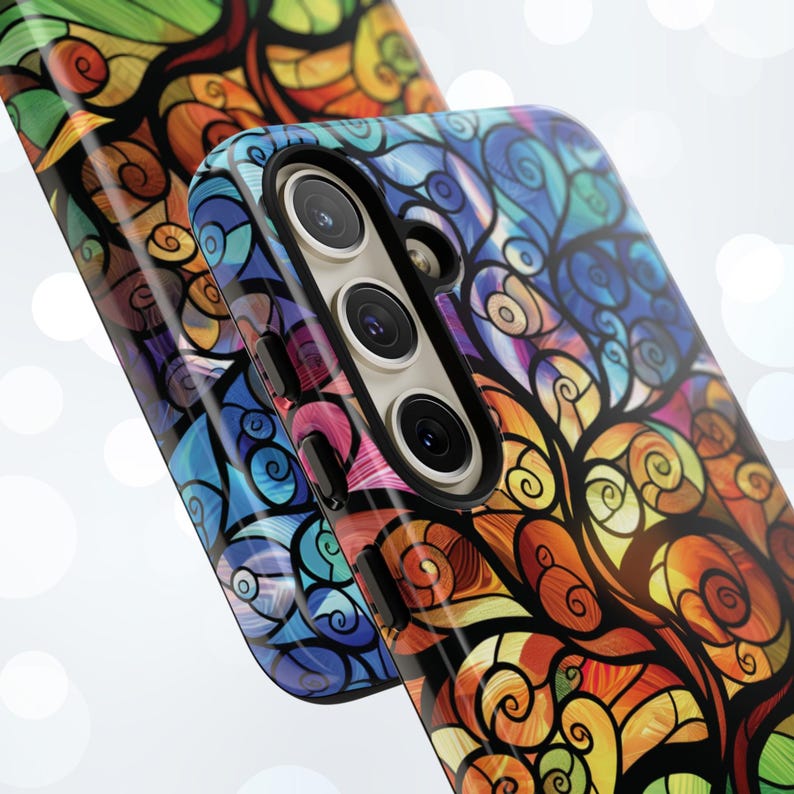 May include: A colorful phone case with a stained glass design featuring swirls and a tree. The case has a black camera bump with three lenses.
