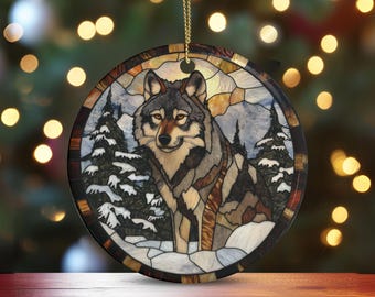 Könnte beinhalten: Runder Weihnachtsschmuck mit einem Wolf in einer verschneiten Waldszene, im Stil eines Glasfensters gestaltet. Er hat eine goldene Kette zum Aufhängen. Der Wolf hat graues, braunes und weißes Fell, umgeben von schneebedeckten Tannen.