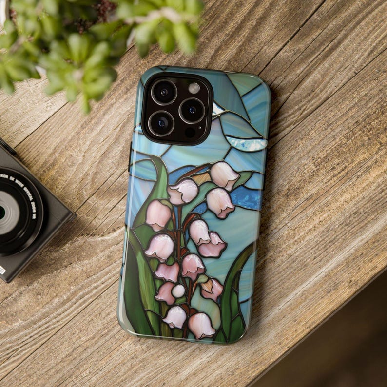Pu&ograve; includere: Una custodia per telefono con un design in vetro colorato che presenta un bouquet di gigli bianchi su uno sfondo blu.