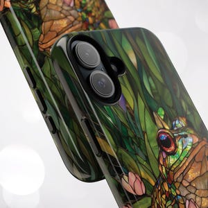 May include: A phone case with a stained glass design featuring a frog and green leaves. The case has a black border and a camera lens cutout.