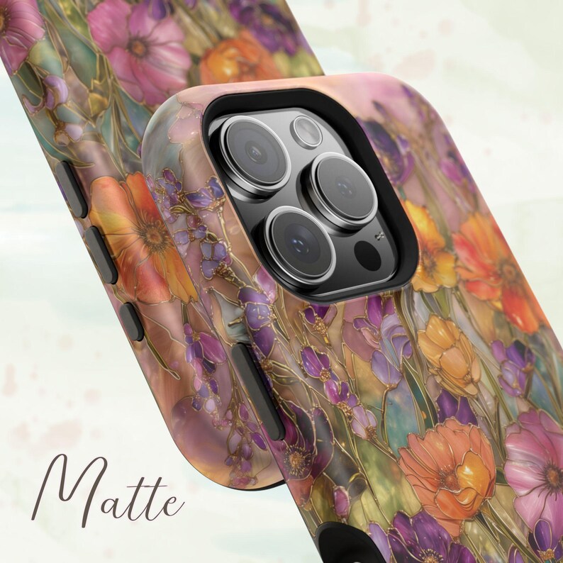 Op de afbeelding: Matte telefoonhoes met een bloemenpatroon in roze, oranje, paarse en gele tinten. De hoes heeft een zwarte cameralensrand en het woord "Matte" staat op de hoes.