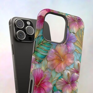 May include: A smartphone case featuring a vibrant floral pattern of pink, orange, and purple hibiscus flowers with green leaves, all outlined in gold. The case has a large cutout for the camera module and is shown next to a dark gray smartphone.