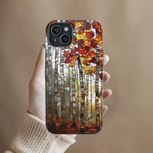 May include: A smartphone case featuring a stained-glass design of a forest scene. The case showcases birch trees with white bark and vibrant autumn leaves in shades of red, orange, and yellow. The design is set against a neutral background.