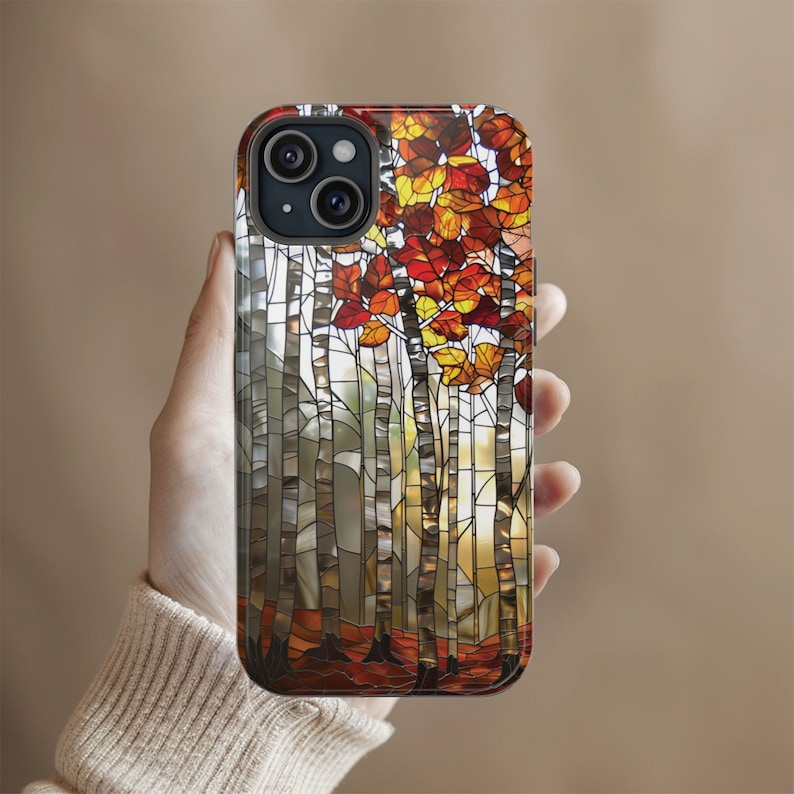 May include: A smartphone case featuring a stained-glass design of a forest scene. The case showcases birch trees with white bark and vibrant autumn leaves in shades of red, orange, and yellow. The design is set against a neutral background.