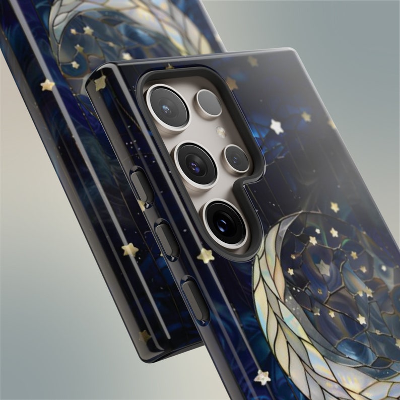 Puede incluir: Una funda de tel&eacute;fono negra con un dise&ntilde;o de luna y estrellas de vidrio emplomado dorado y azul. La funda tiene una protuberancia de c&aacute;mara elevada con tres lentes.