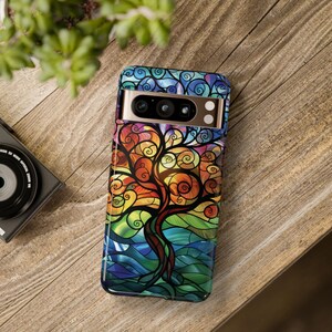 May include: A colorful phone case with a stained glass design of a tree with swirling branches. The case is designed for a phone with a triple camera lens.
