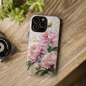 K&ouml;nnte beinhalten: Eine Handyh&uuml;lle mit einem Blumendesign mit rosa Pfingstrosen auf wei&szlig;em Hintergrund. Die H&uuml;lle hat einen Kameraausschnitt mit drei Objektiven.