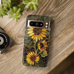 May include: A phone case with a stained glass design featuring three yellow sunflowers with brown centers. The case has a camera cutout with a gold trim.