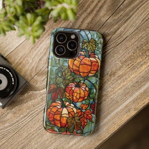 May include: A phone case with a stained glass design featuring pumpkins, leaves, and vines in shades of orange, green, and blue.