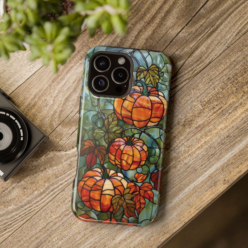 May include: A phone case with a stained glass design featuring pumpkins, leaves, and vines in shades of orange, green, and blue.