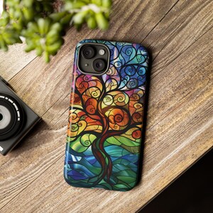 May include: A colorful phone case with a stained glass design of a tree with swirling branches. The case is made of durable plastic and features a raised camera bump for protection.