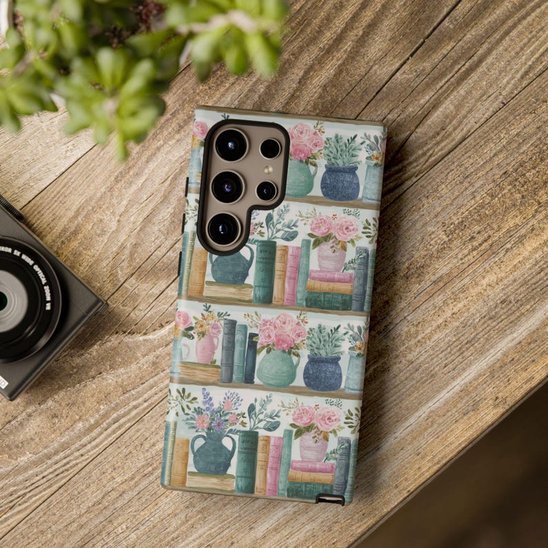 Peut inclure: Coque de t&eacute;l&eacute;phone avec un motif de biblioth&egrave;que, pr&eacute;sentant des vases de fleurs et des piles de livres. Le bo&icirc;tier a un fond blanc avec un motif r&eacute;p&eacute;t&eacute; d'&eacute;tag&egrave;res, de livres et d'arrangements floraux roses, bleus et verts.