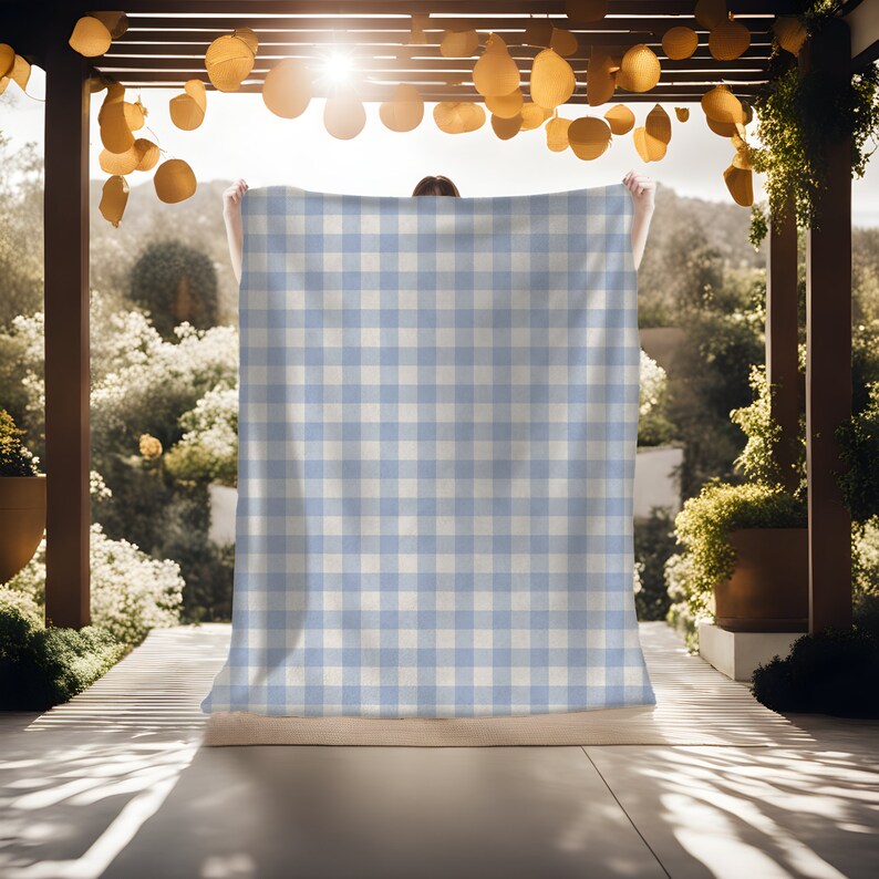 May include: A light blue and white gingham check picnic blanket. The blanket is being held up by a person in a sunny outdoor setting.