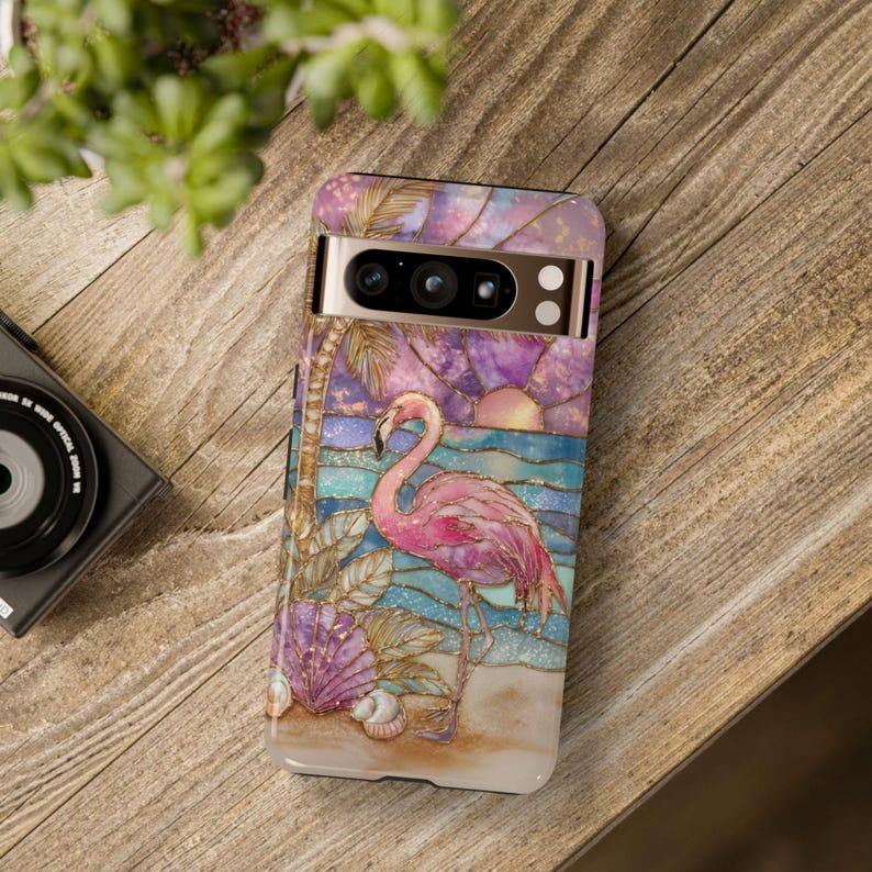 Puede incluir: Una funda de tel&eacute;fono con un dise&ntilde;o de flamenco. La funda tiene una colorida ilustraci&oacute;n de un flamenco rosa en una playa con un atardecer y un fondo de oc&eacute;ano. La funda est&aacute; dise&ntilde;ada para un tel&eacute;fono con c&aacute;mara y flash.