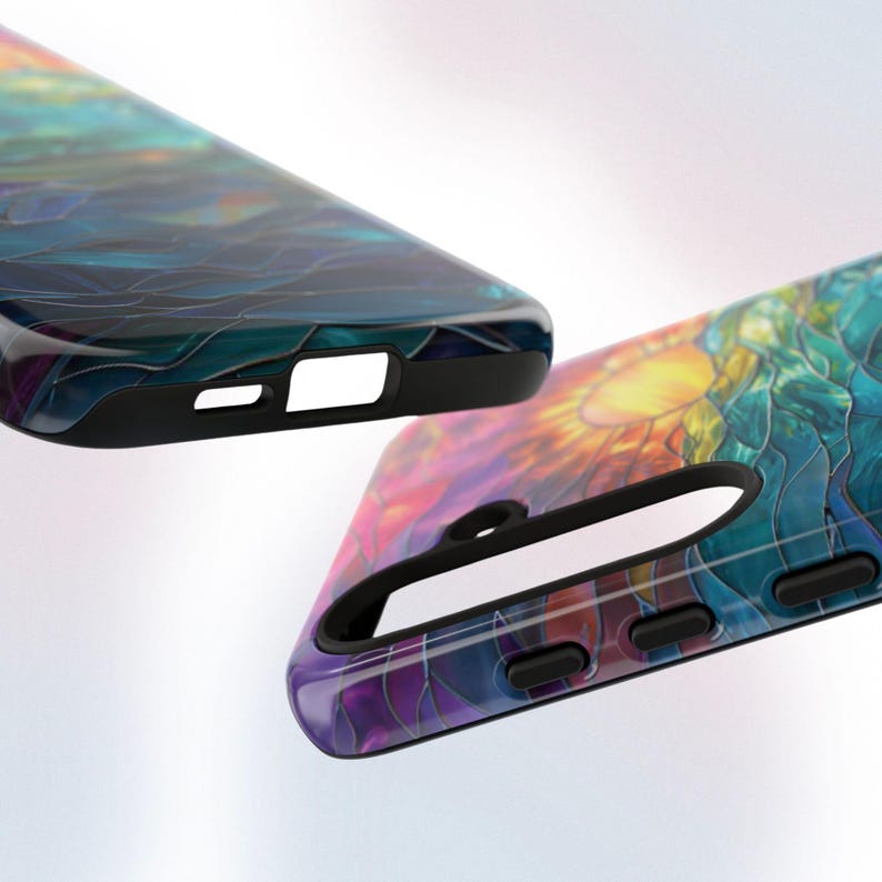 Pu&ograve; includere: Una custodia per telefono colorata con un design a vetri colorati che rappresenta un'alba sopra una catena montuosa. La custodia ha un bordo nero e un ritaglio per l'obiettivo della fotocamera.