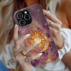 May include: A phone case with a celestial design. It features a golden sun and crescent moon against a backdrop of purple clouds and stars. The case has a glossy finish and a protective bumper.