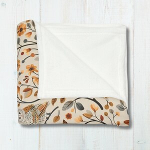 May include: A soft, plush throw blanket with a white fleece backing and a printed front featuring a stylized owl, branches, and leaves in shades of brown, yellow, and gray.