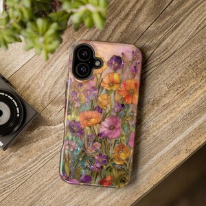 Op de afbeelding: Een telefoonhoesje met een bloemenontwerp met oranje, paarse en roze bloemen. De hoes heeft een glanzende afwerking en staat op een houten achtergrond. Het ontwerp toont gedetailleerde bloemblaadjes en bladeren.