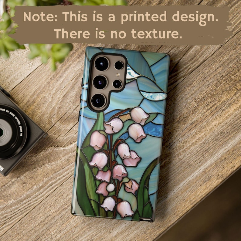 Pu&ograve; includere: Una custodia per telefono blu e verde con un design a vetri colorati di mughetti. La custodia ha un bordo nero e un ritaglio per la fotocamera.