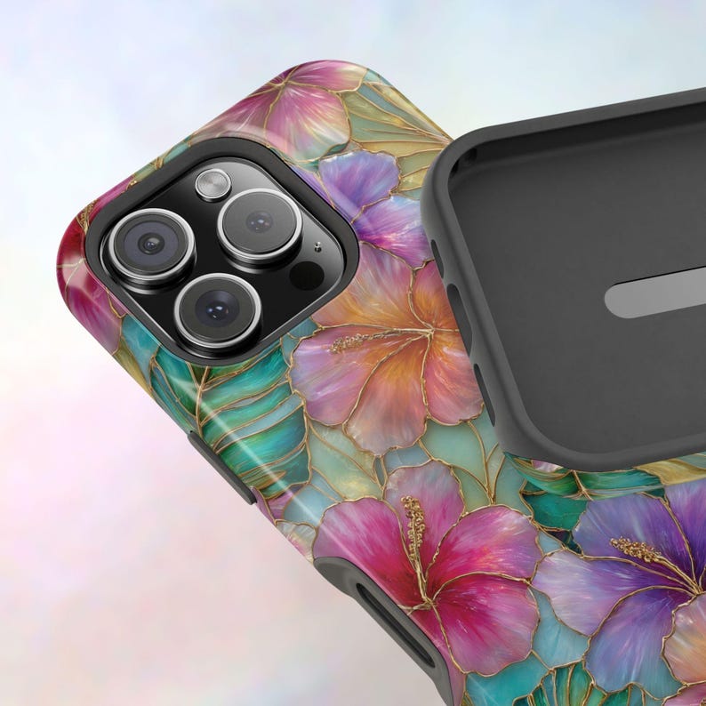 May include: A protective phone case featuring a vibrant floral pattern with pink, purple, and orange hibiscus flowers accented by teal tropical leaves and thin gold outlines. The case has a black interior lining and a triple camera cutout.