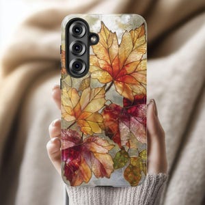 May include: A smartphone case featuring a stained-glass design of autumn leaves in shades of red, orange, and yellow. The case has a marble-like background and a triple-lens camera cutout.