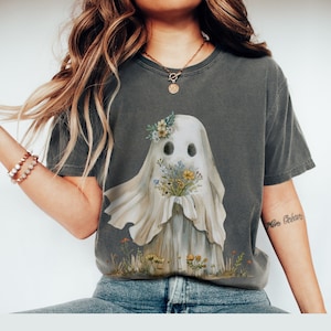 May include: A gray t-shirt with a graphic of a white ghost holding a bouquet of flowers. The ghost has a floral crown and a friendly face.