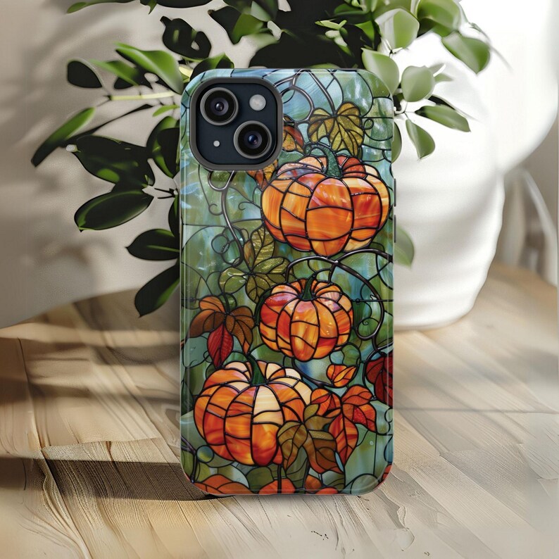 May include: A stained glass style phone case with a design of orange pumpkins on a vine with green leaves.