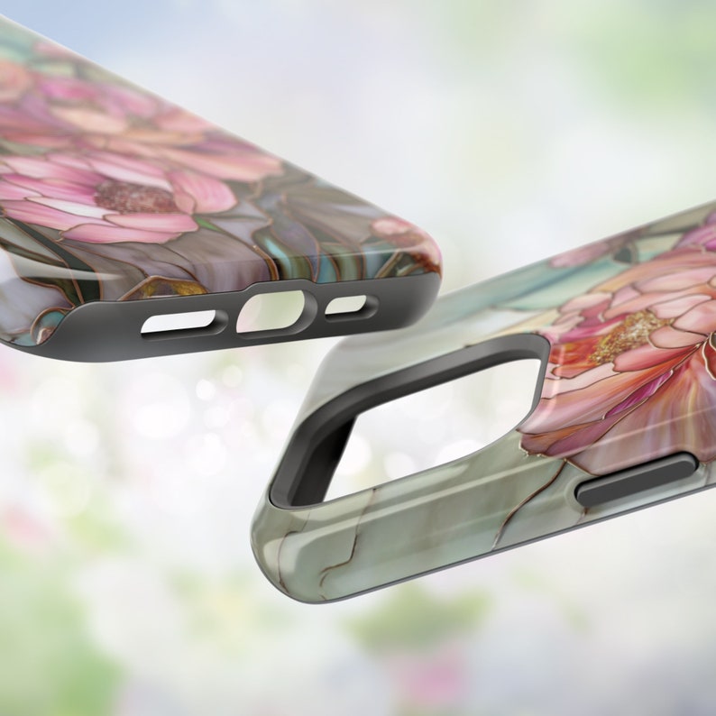 May include: Two phone cases with a floral design. The cases are gray and have a raised edge around the camera lens. The floral design is pink, white, and gold.