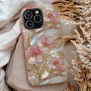 May include: A phone case with a floral design. The case features pink flowers with gold-colored outlines and light green leaves against a white background. The case has a pearlescent effect, giving it a shimmering appearance.