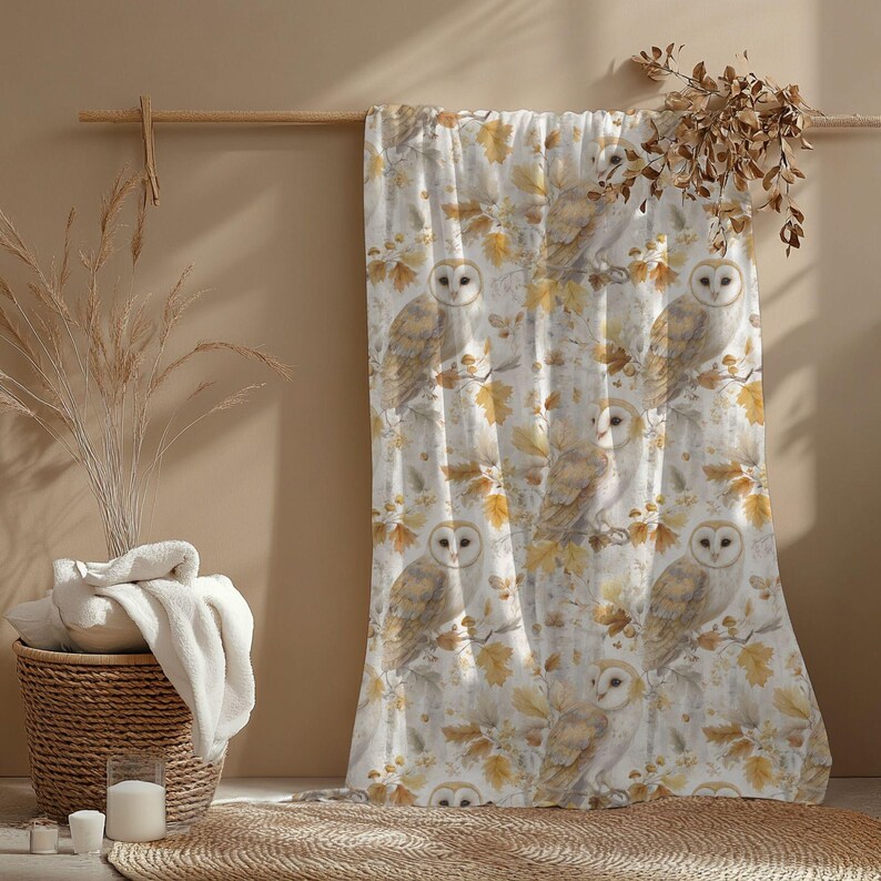 May include: A white and beige patterned curtain with watercolour illustrations of owls on branches with autumn leaves. The curtain hangs on a wooden rod. A woven basket and candles are in the foreground.