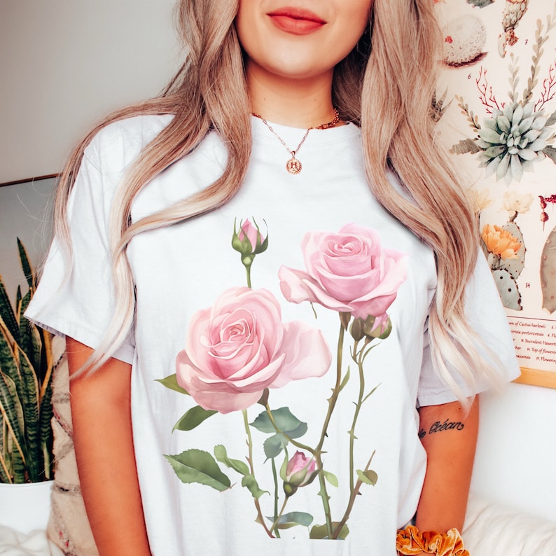 May include: White t-shirt with a pink rose floral print. The roses are pink with green leaves and stems.