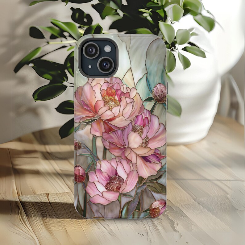 May include: A phone case with a stained glass design featuring pink peonies and green leaves. The case has a cutout for the camera lens.