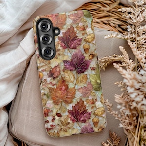 May include: A rectangular smartphone case featuring a mosaic-style pattern of autumn leaves in shades of deep red, orange, gold, and brown. The design includes small acorns and berries scattered among the foliage, with a black camera lens cutout.