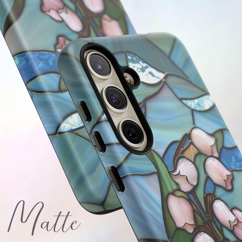 Pu&ograve; includere: Una custodia per telefono blu e bianca con un design a vetri colorati con fiori rosa. La custodia ha una finitura opaca e un ritaglio per la fotocamera.