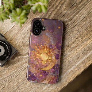 May include: A smartphone case with a celestial design. It features a gold sun and crescent moon set against purple and orange clouds. The case has a glossy finish. The case is designed to fit a smartphone.