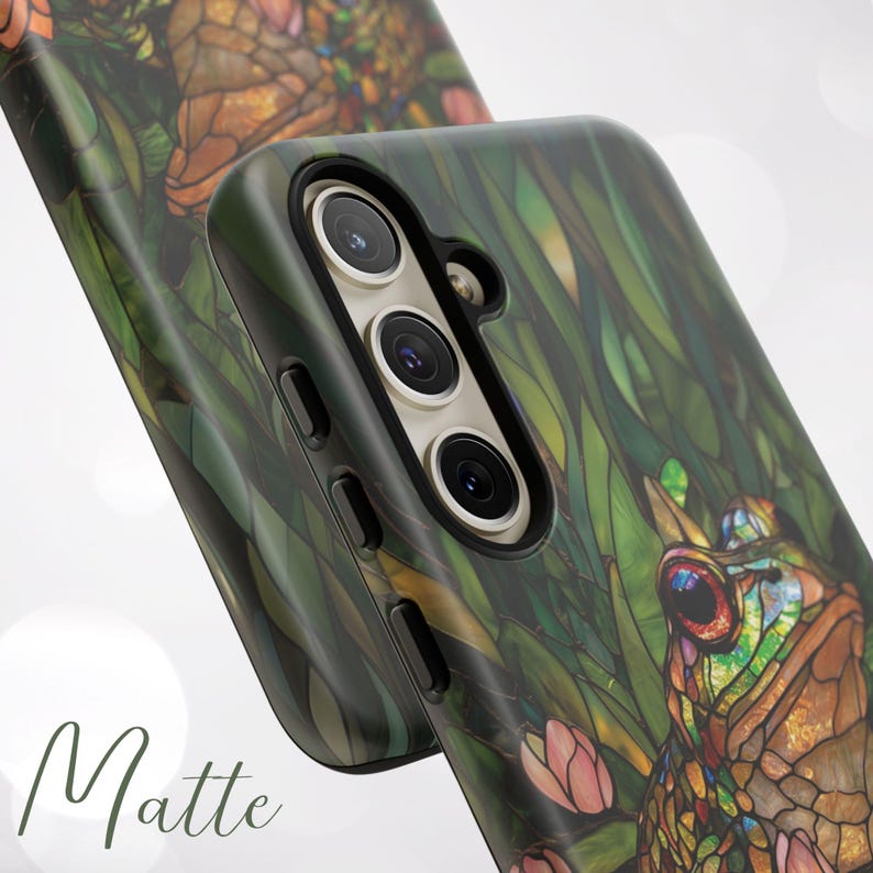 May include: A green, brown, and blue phone case with a stained glass design of a frog and flowers. The case has a matte finish and a camera cutout.