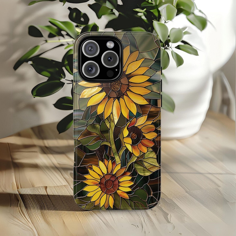 May include: A phone case with a stained glass design featuring sunflowers in shades of yellow, brown, and green.