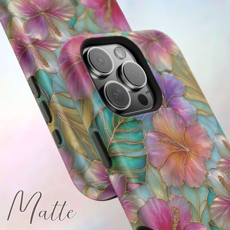 May include: A smartphone case featuring a floral pattern with pink and orange hibiscus flowers, teal leaves, and gold outlines. The case has a matte finish and a black camera cutout area with three circular lenses and a flash. The word Matte is visible.