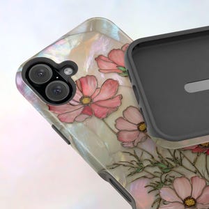 May include: A phone case with a floral design. The case features pink flowers with yellow centers and green stems against a pearlescent background. The case has a black interior and a dual-lens camera cutout.