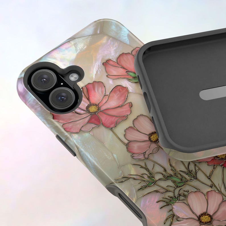 May include: A phone case with a floral design. The case features pink flowers with yellow centers and green stems against a pearlescent background. The case has a black interior and a dual-lens camera cutout.