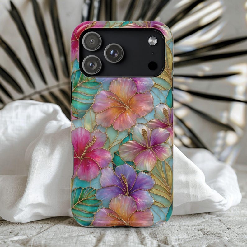 May include: A smartphone case featuring a vibrant floral pattern with hibiscus flowers in shades of pink, purple, orange, and yellow. The design includes green tropical leaves and gold-colored outlines, creating a stained-glass effect.