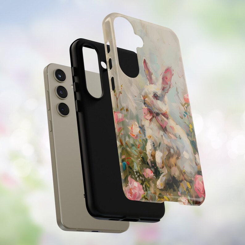 K&ouml;nnte beinhalten: Eine Handyh&uuml;lle mit einer Illustration eines wei&szlig;en Kaninchens, umgeben von rosa und gr&uuml;nen Blumen. Die H&uuml;lle ist aus hartem Kunststoff und hat einen schwarzen Rand.