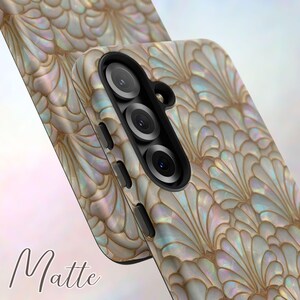 May include: A matte phone case with a pearlescent, fan-shaped design in shades of white, gold, and iridescent hues. The case features a triple-lens camera cutout and side buttons. The word "Matte" is printed in a cursive font.