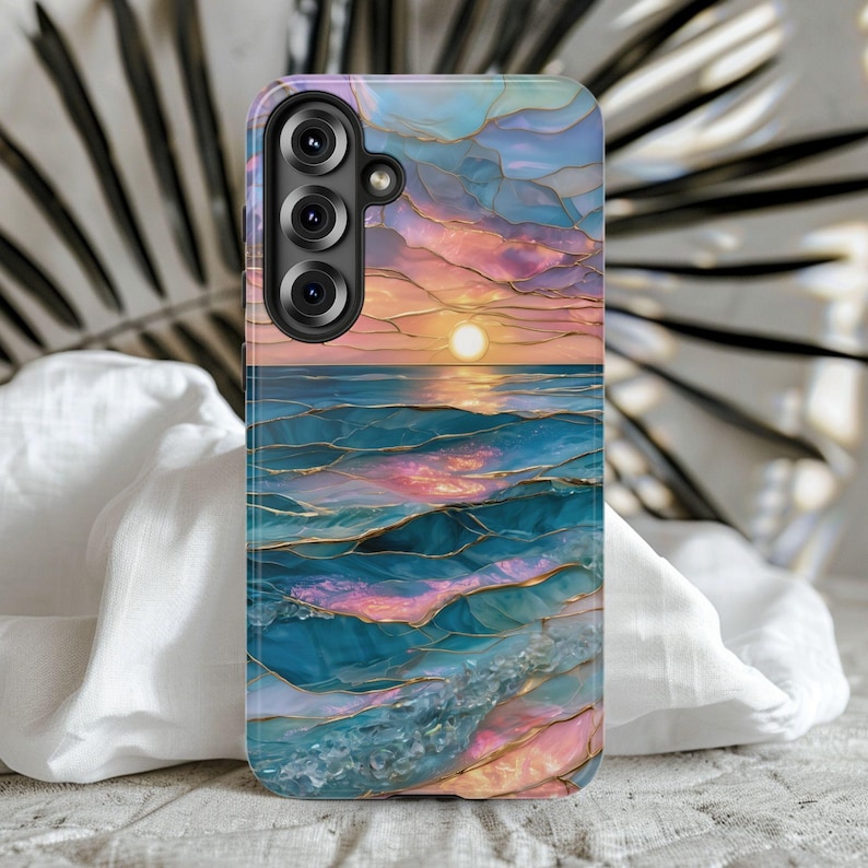 May include: A phone case featuring a sunset over the ocean design. The case has a colorful, abstract design with shades of blue, pink, and gold. The case has a camera module with three lenses.
